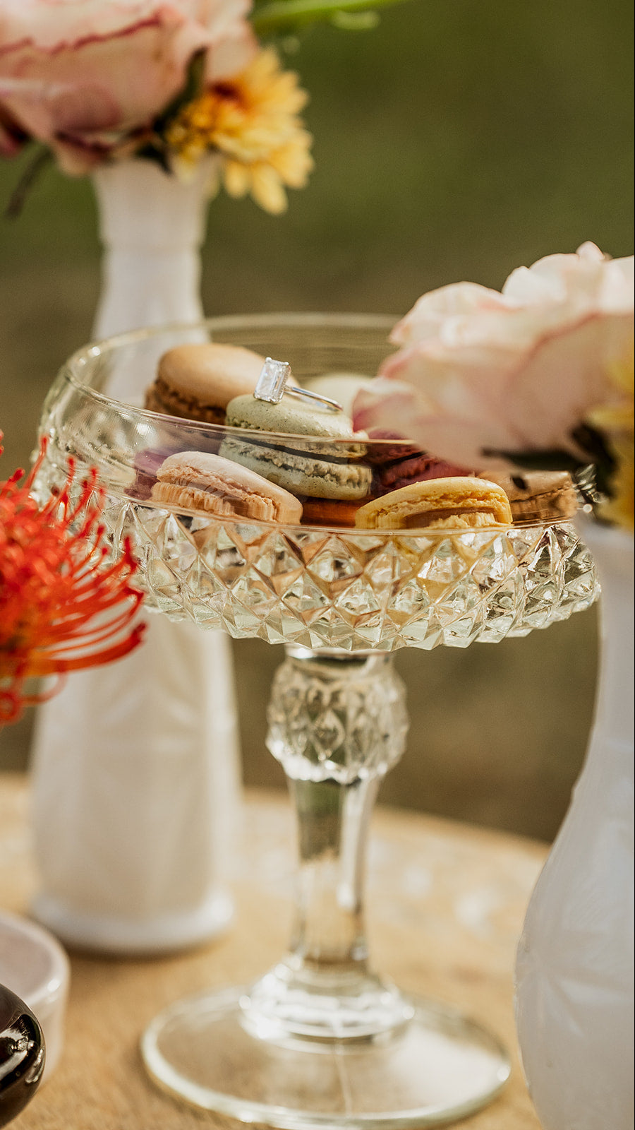 Glass stand with macarons and flowers on a blurred background.  asheville luxury picnics. pop-up picnic. picnic pop-up avl