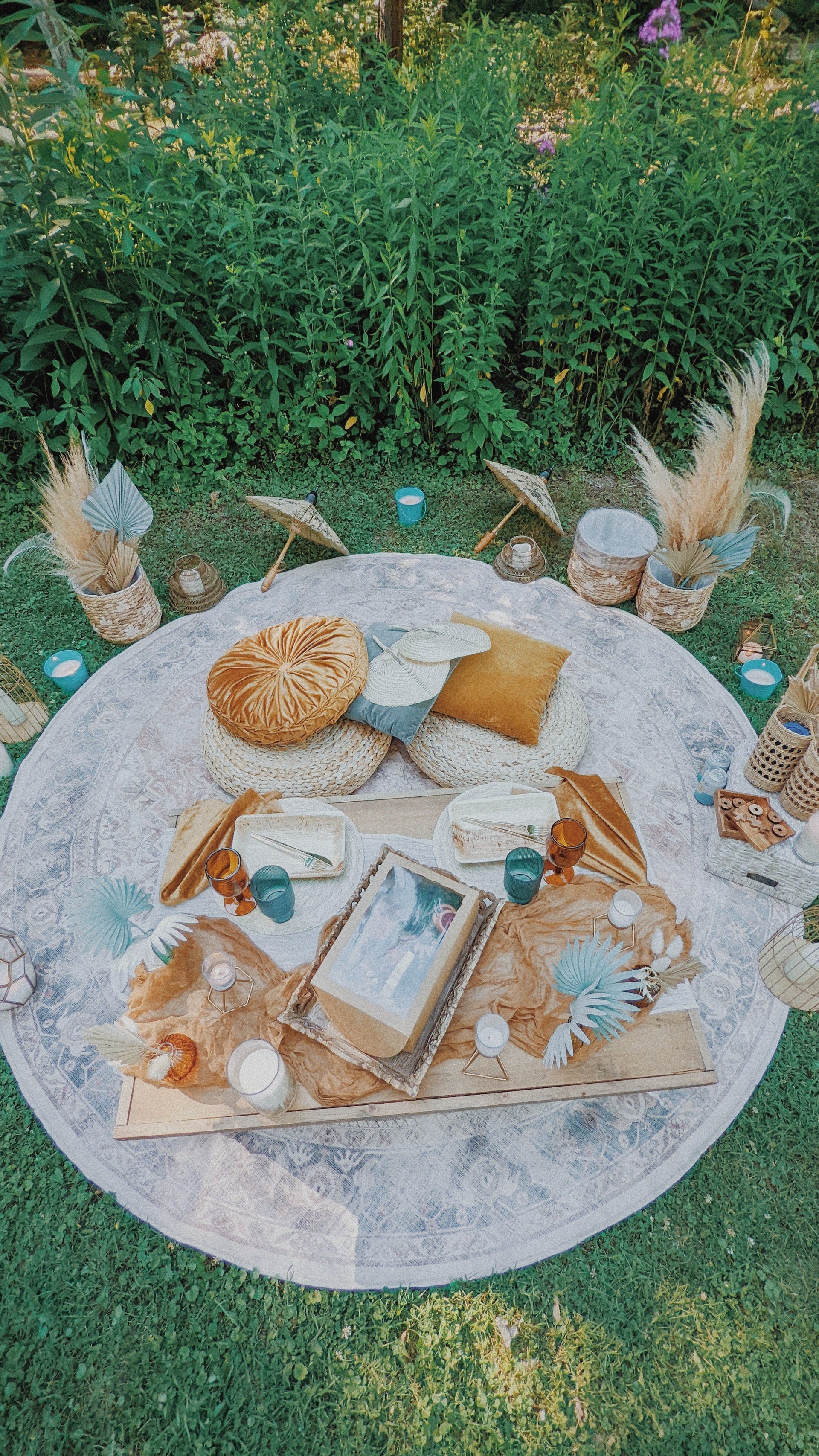 Decorative outdoor setup with a round rug, pillows, and various items on a grassy area. asheville luxury picnics. pop-up picnic. picnic pop-up avl