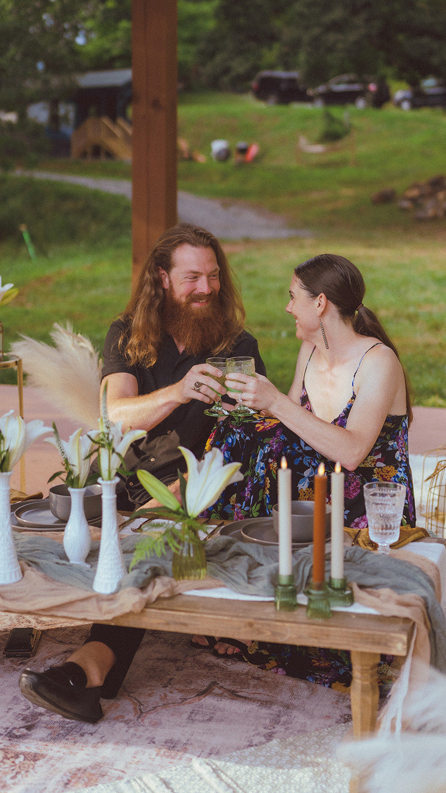 Two people sitting at a table outdoors with candles and decorative items. Asheville Luxury Picnics picnic pop up avl