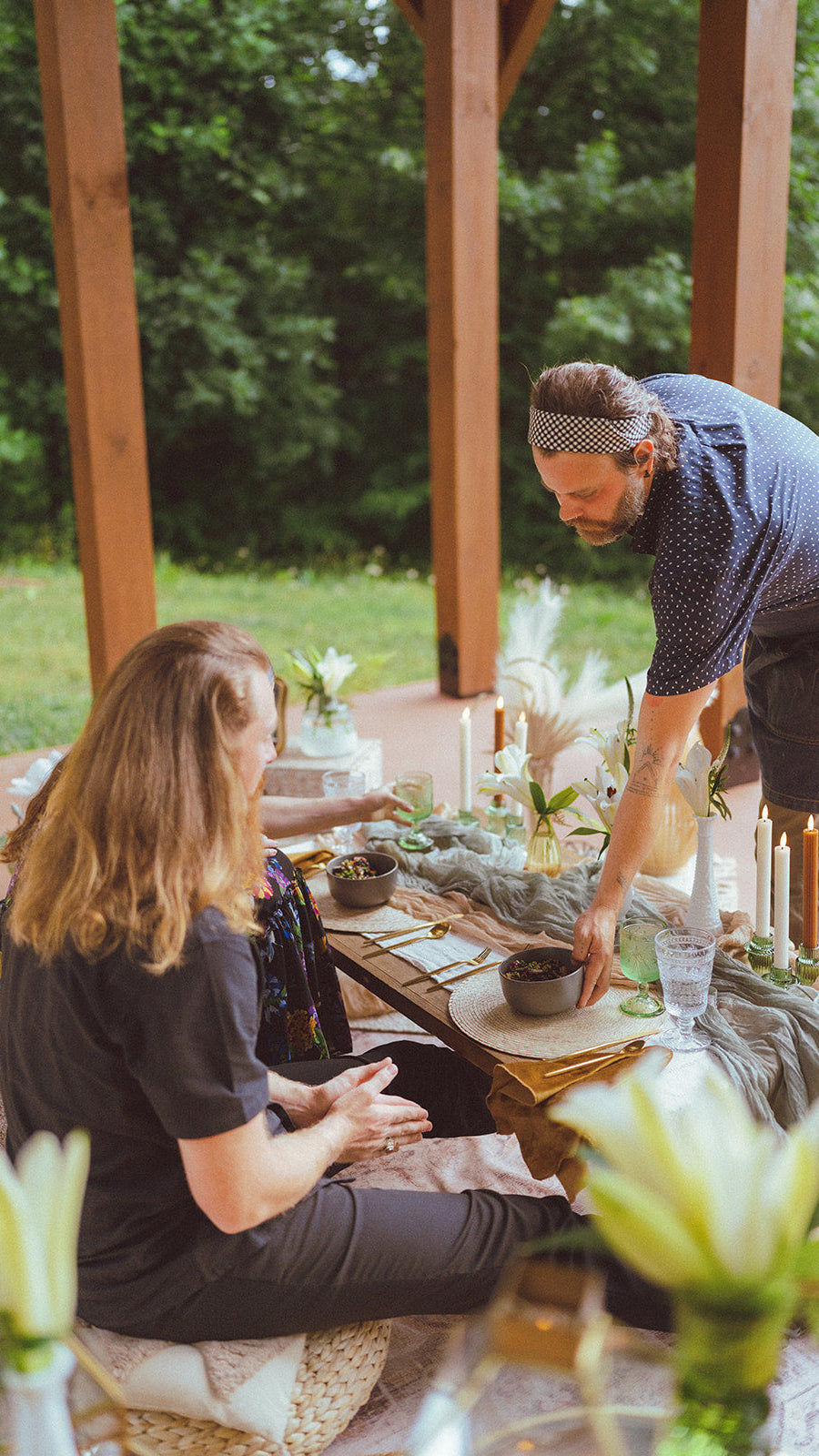Two people setting up a table outdoors with candles and plants. cute picnic country couple avl