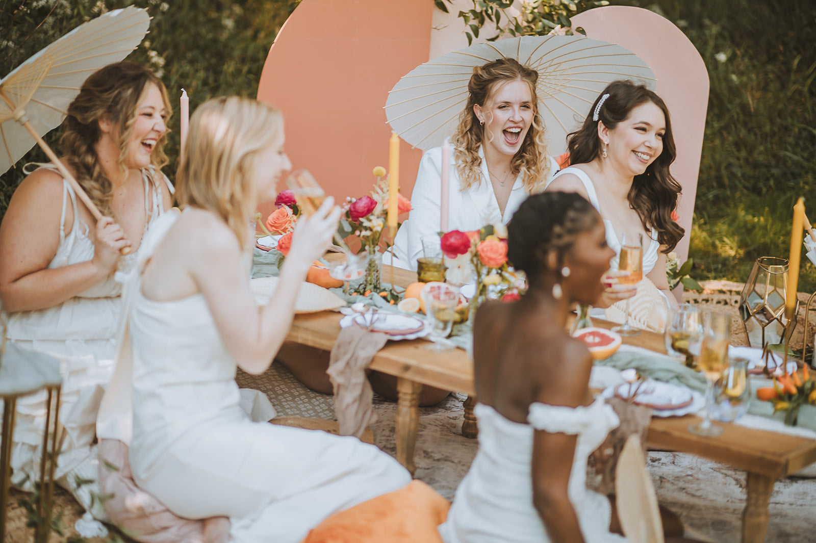Group of women sitting around a table with a large photo of four women on a heart-shaped board behind them. Bachelorette. Asheville Luxury Picnics. Picnic Pop-Up. AVL 