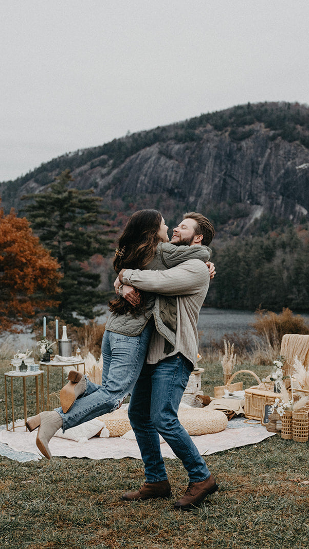 Couple embracing outdoors with a scenic background of mountains and trees. cute picnic country couple avl