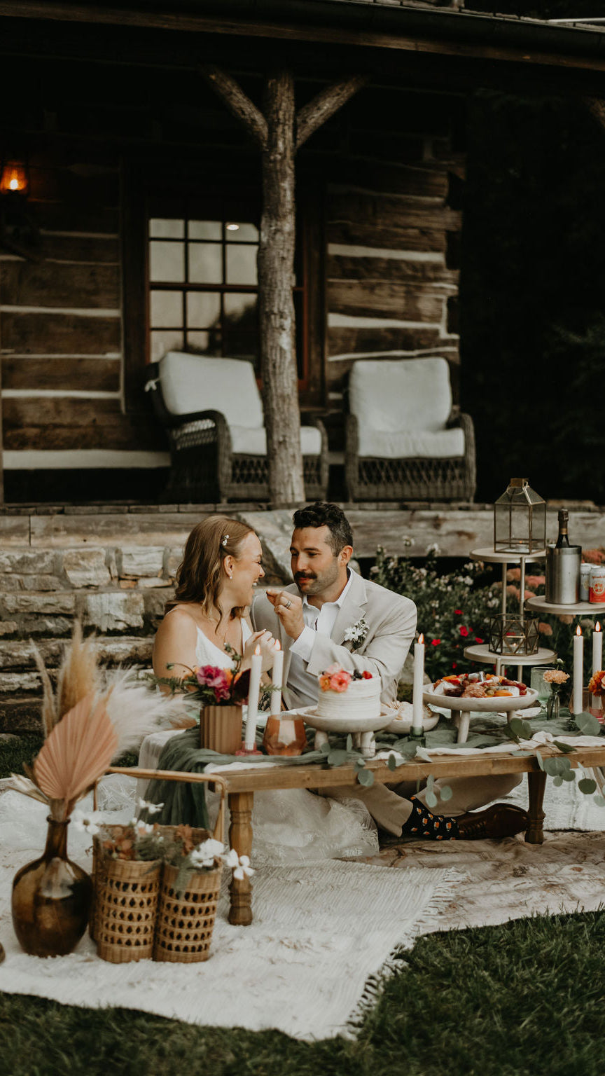 Couple at a rustic outdoor wedding reception with a cake and decorations.  asheville luxury picnics. pop-up picnic. picnic pop-up avl