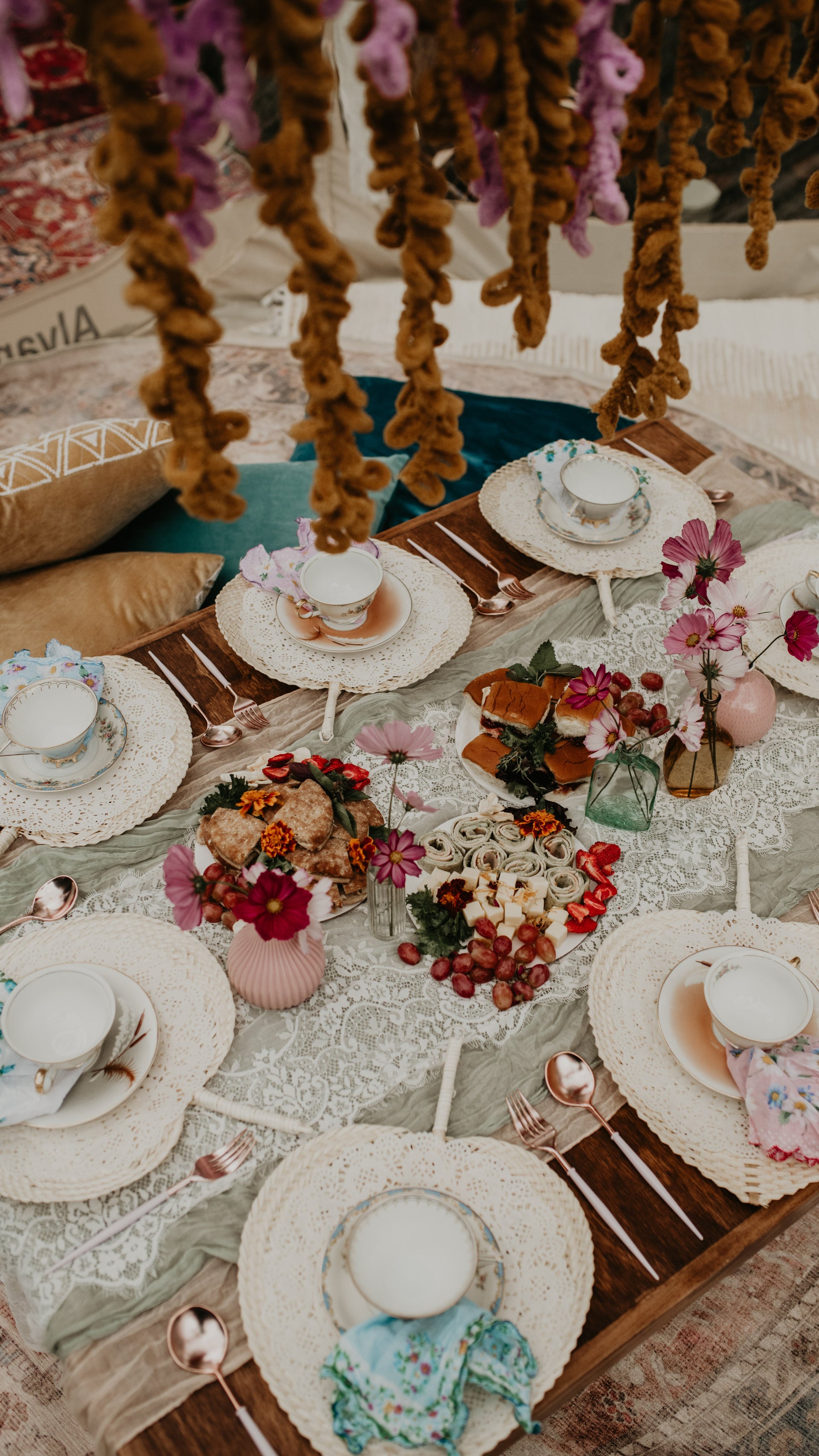 Decorative table setting with floral arrangements and hats on a patterned rug.  asheville luxury picnics. pop-up picnic. picnic pop-up avl