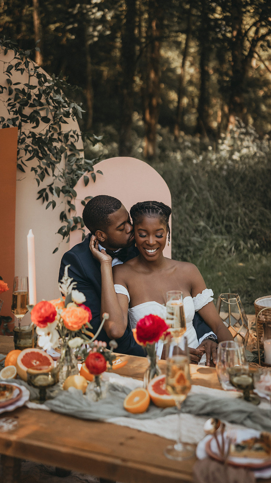Couple sitting at a table with a floral arrangement and candles in an outdoor setting.  asheville luxury picnics. pop-up picnic. picnic pop-up avl.