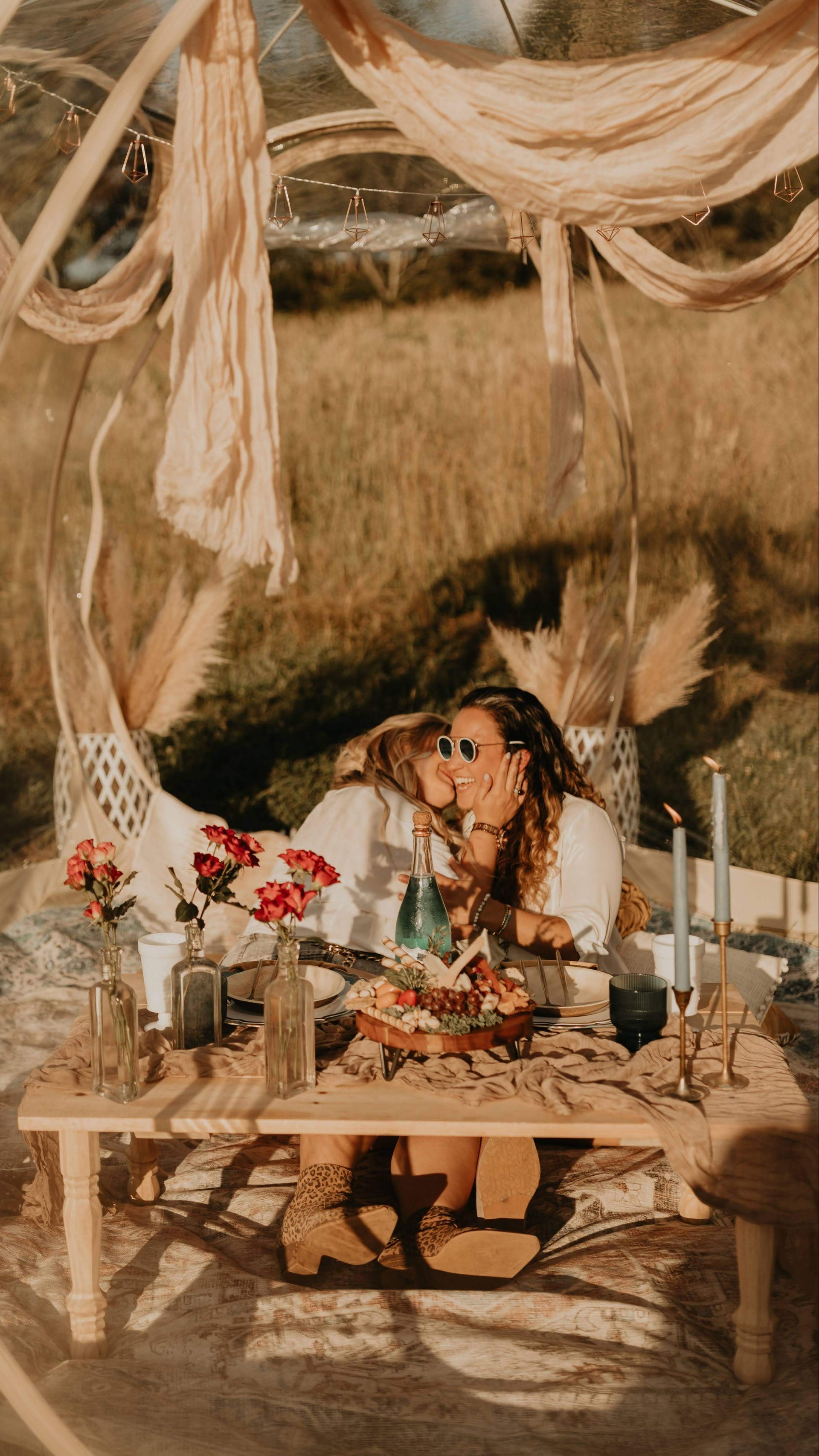 Two people sitting at a table in a natural setting with decorative elements.  asheville luxury picnics. pop-up picnic. picnic pop-up avl