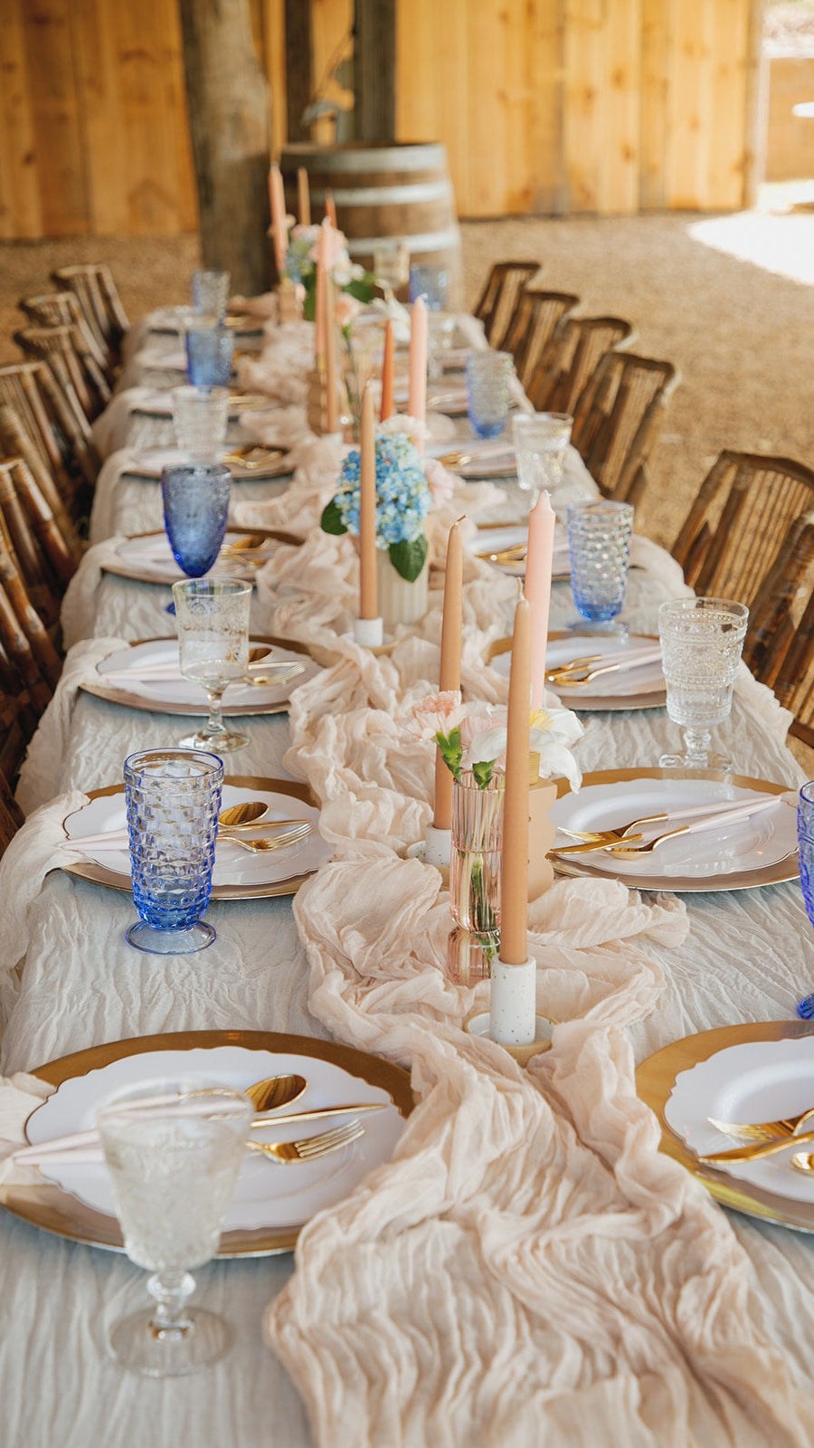 Elegant table setting with blue and clear glassware, white plates, and gold cutlery in a rustic outdoor setting.